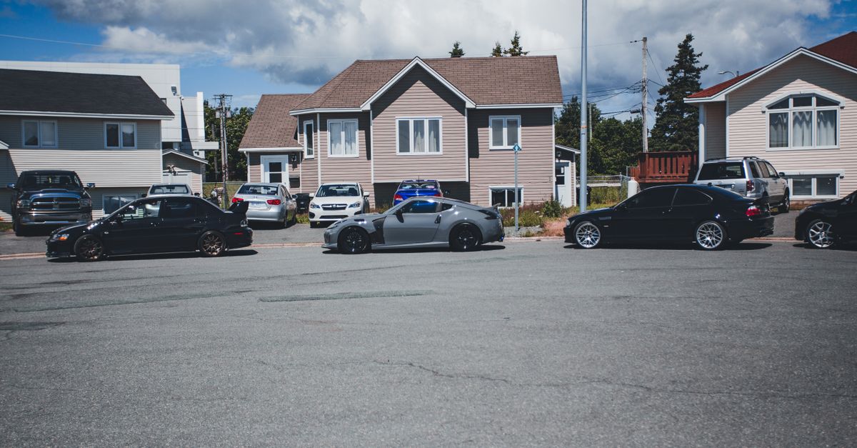 Sunny neighborhood street with modern homes and parked vehicles on a bright day.