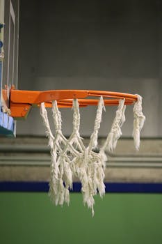 Detailed image of a worn basketball hoop with tangled net in an indoor court.