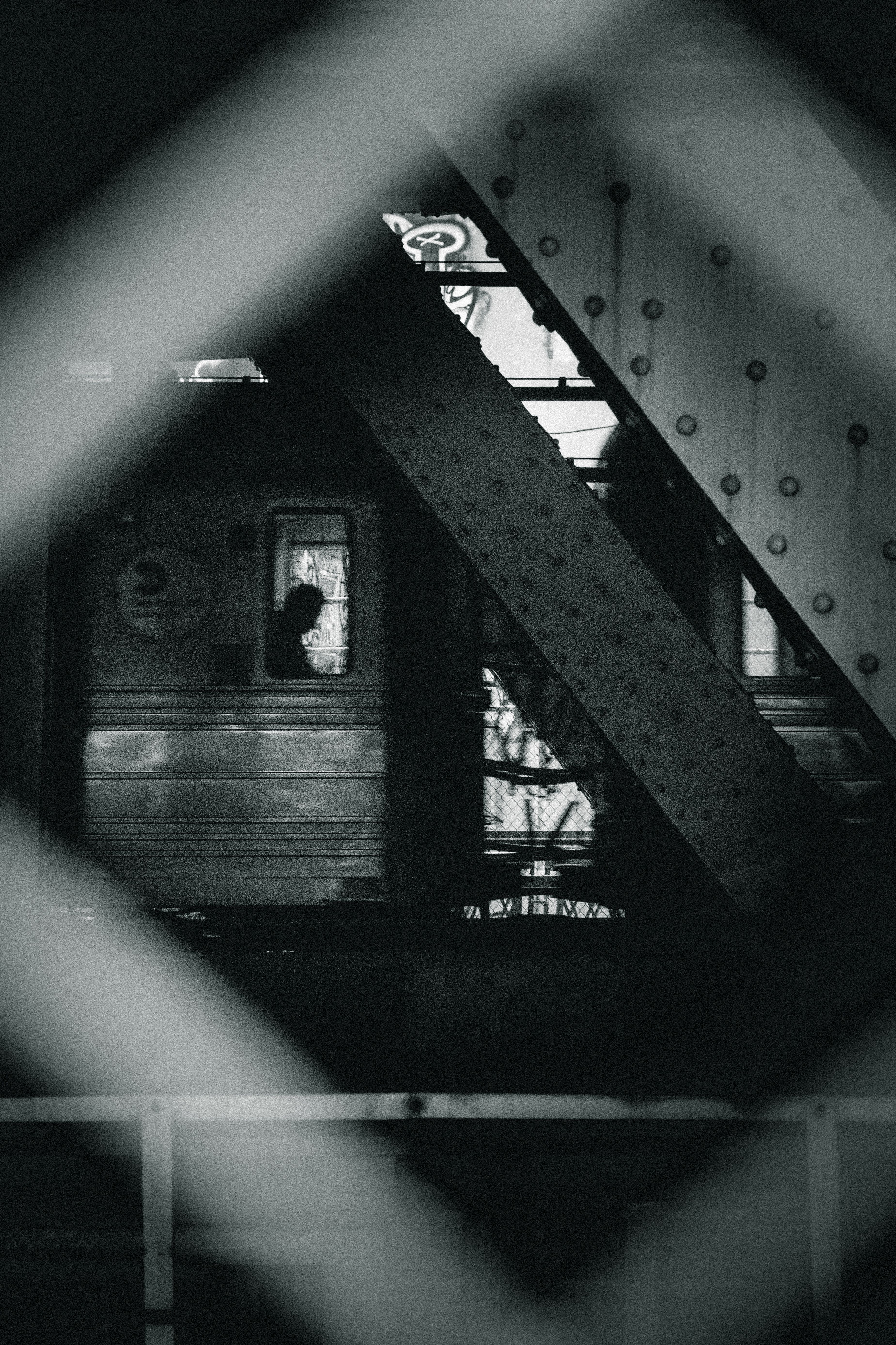 A black and white photo capturing a train with a silhouetted passenger inside, framed by industrial beams.