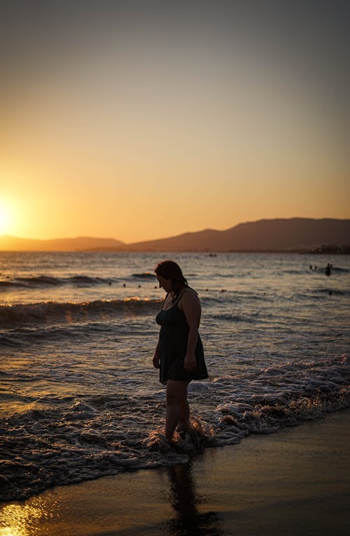 Woman Standing on the Beach during Sunset
