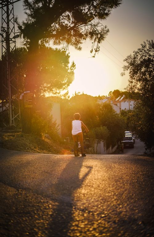 Free A child rides a bicycle down a suburban street at sunset, evoking a sense of freedom and adventure. Stock Photo