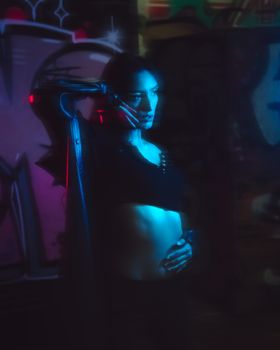 A woman stands in neon lighting against a graffiti wall, creating a moody ambiance.