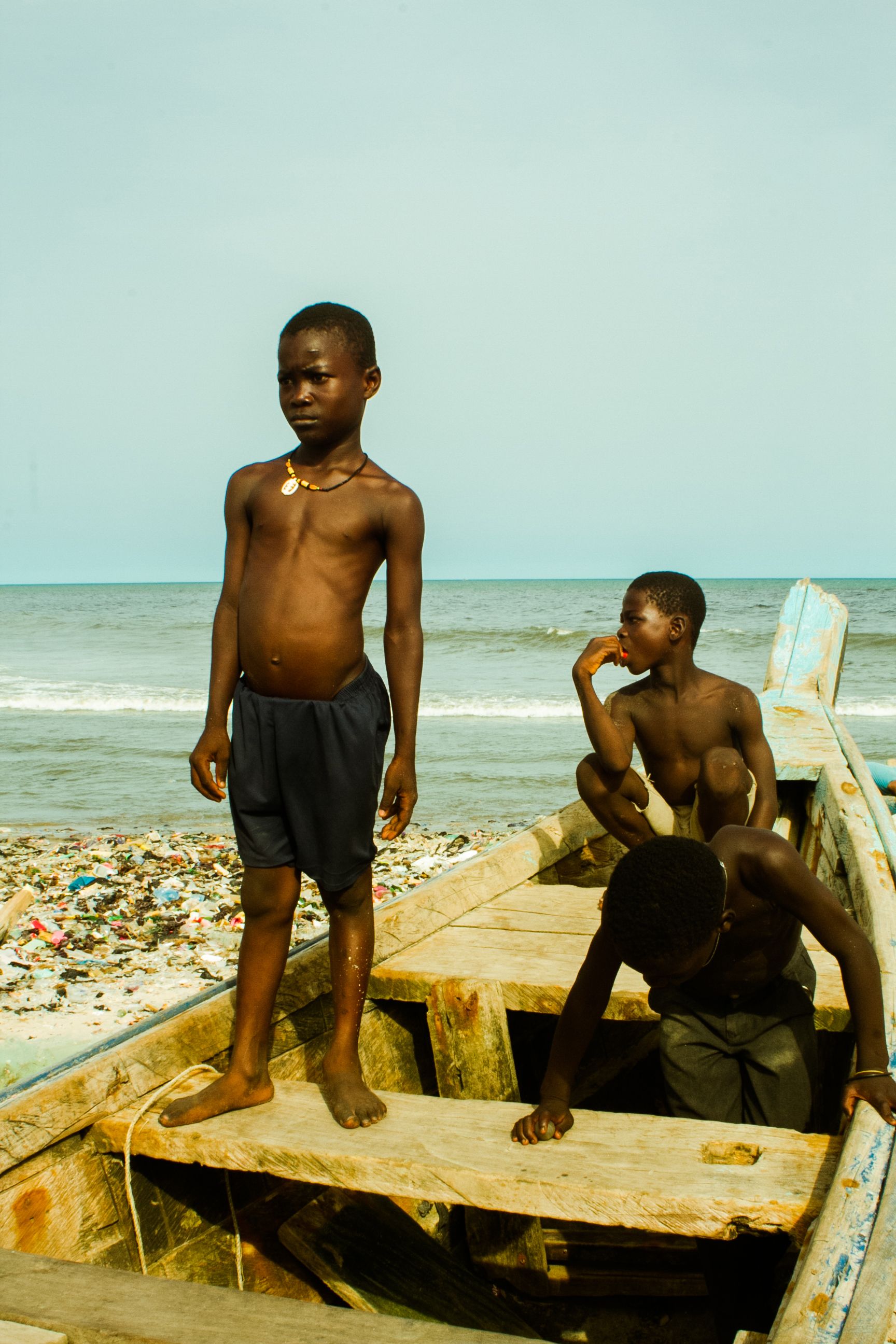 Three boys play on a wooden boat by the sea, embodying adventure and childhood fun.