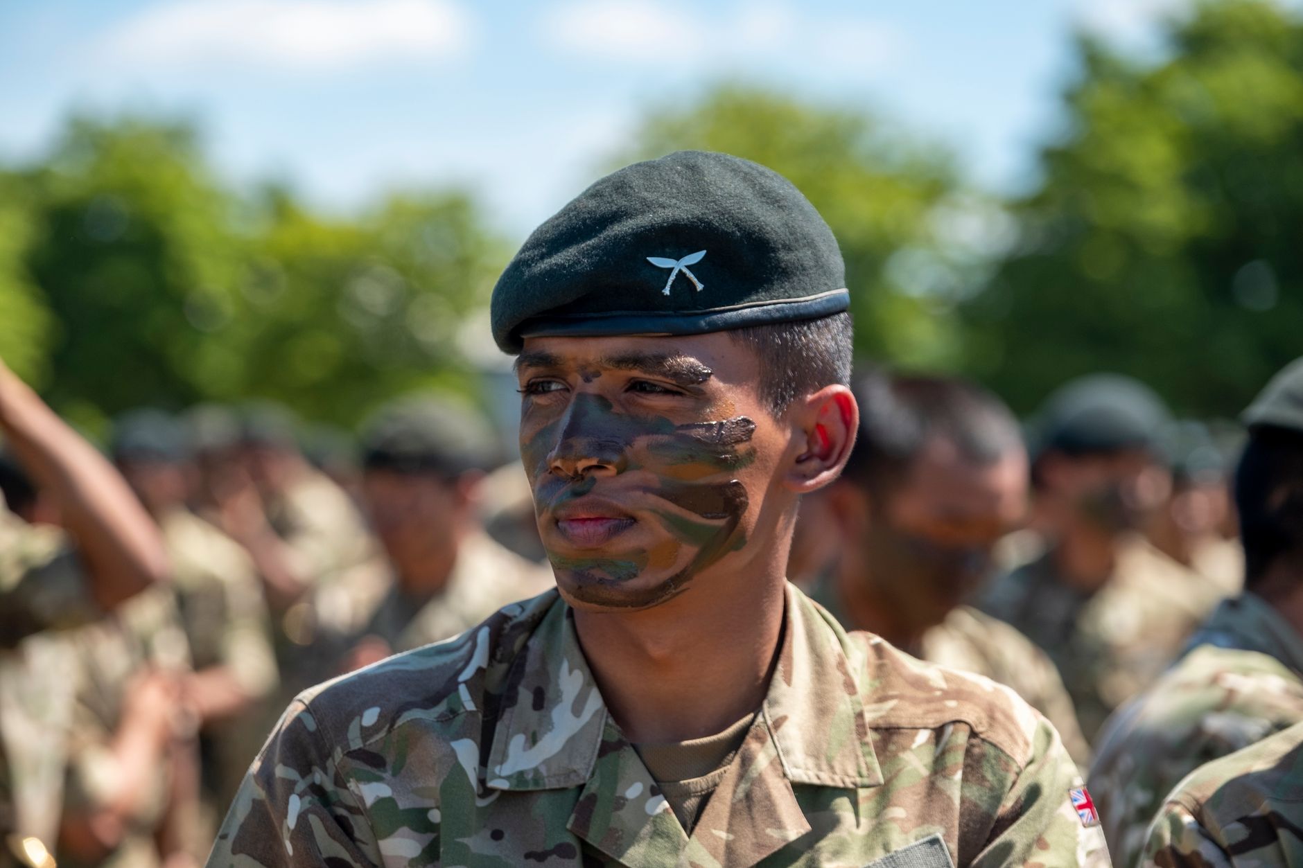 Close-up portrait of a British soldier with face paint, in uniform, standing outdoors in Aldershot, England.