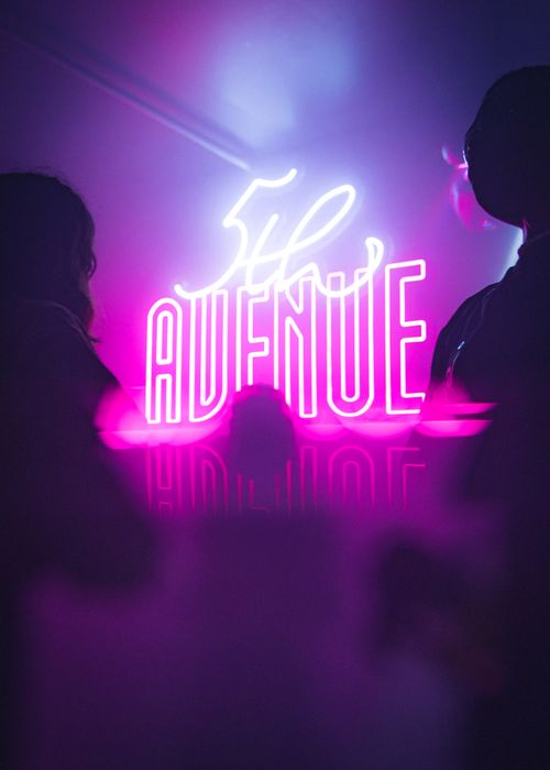 Free Silhouetted figures and a vivid neon 5th Avenue sign capture the Perth nightlife in a vibrant nightclub scene. Stock Photo