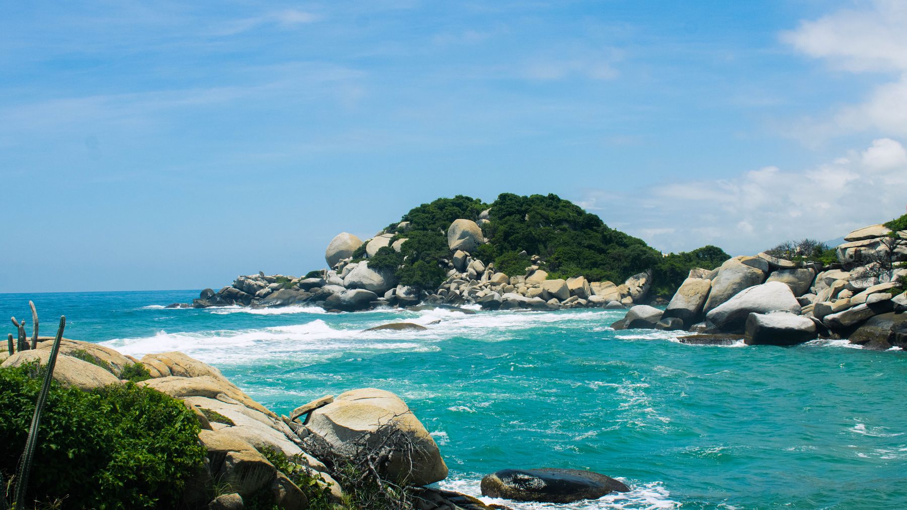 A picturesque view of Tayrona National Park with rocks and turquoise sea under a blue sky.
