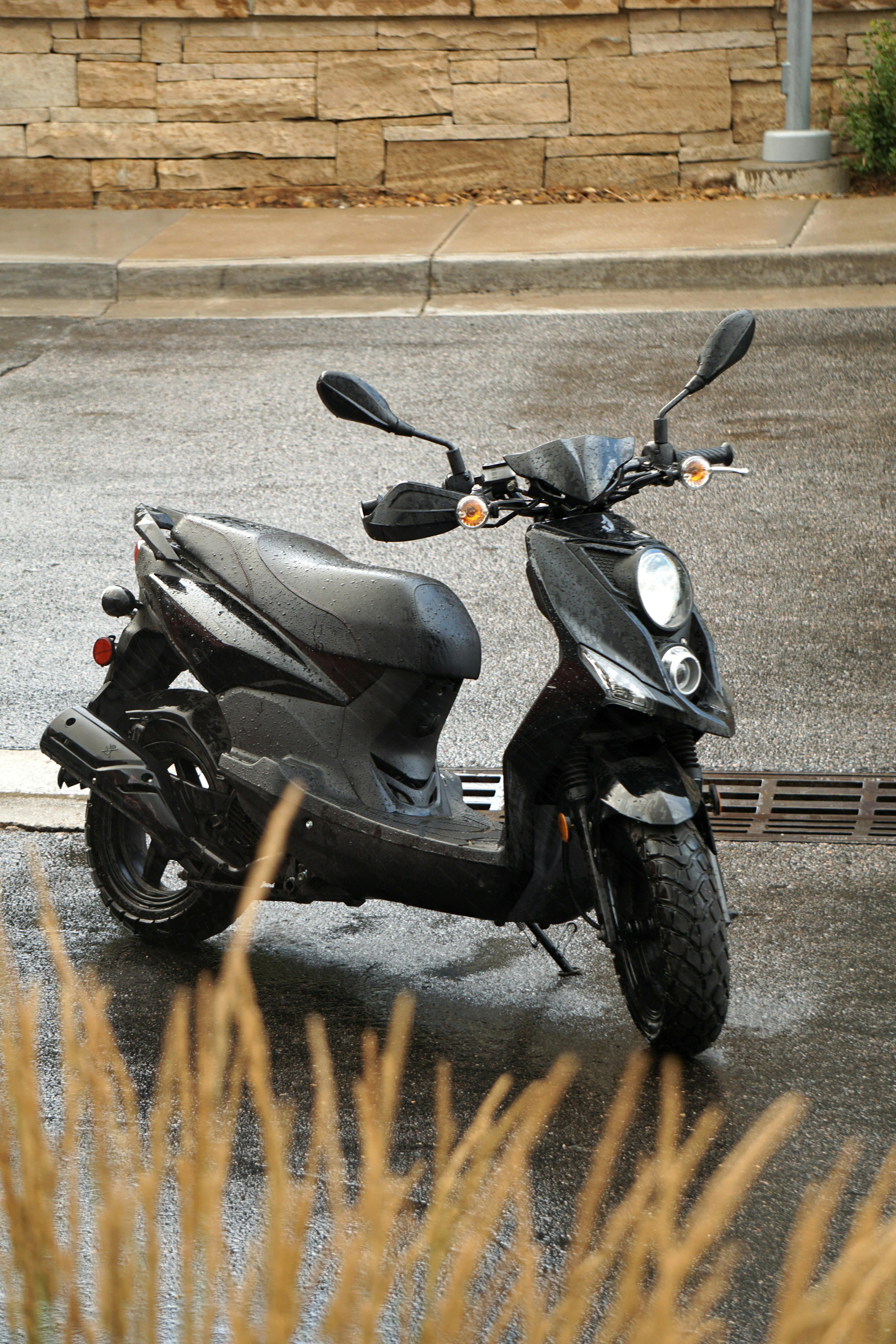 A black scooter parked on a wet street after rain, showcasing urban transportation.