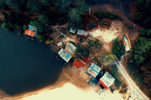 Free Aerial view of a rustic lakeside village with colorful rooftops and surrounding trees. Stock Photo