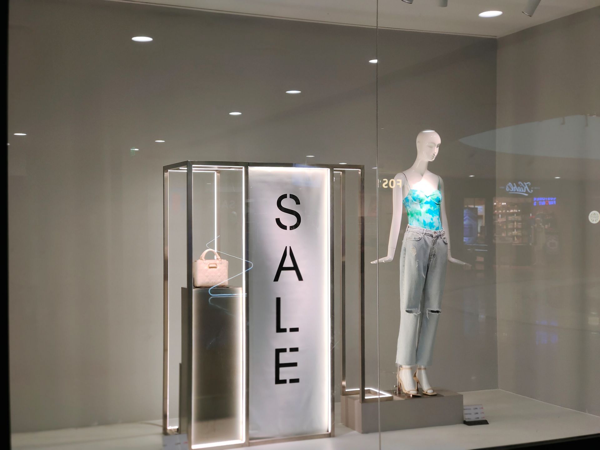 Stylish window display featuring sale sign and fashionable mannequin in trendy outfit.