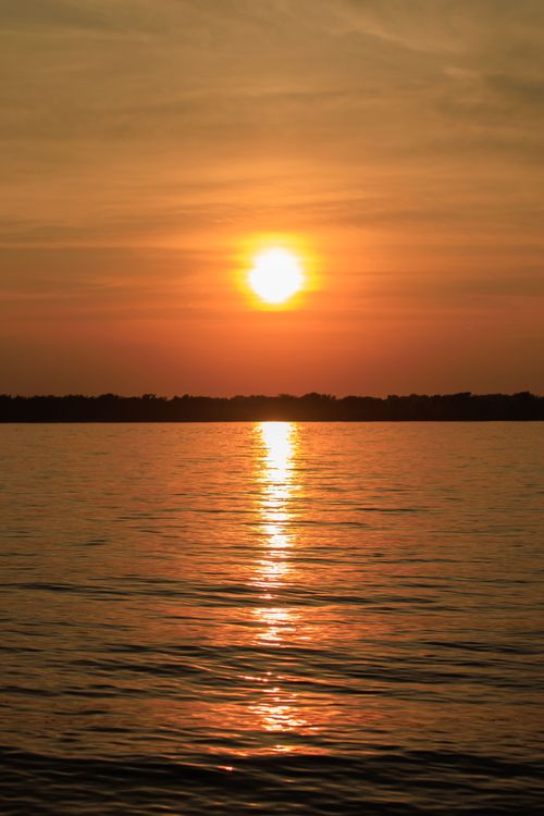 Free A stunning sunset casting vibrant colors over a calm lake, creating a peaceful and scenic view. Stock Photo