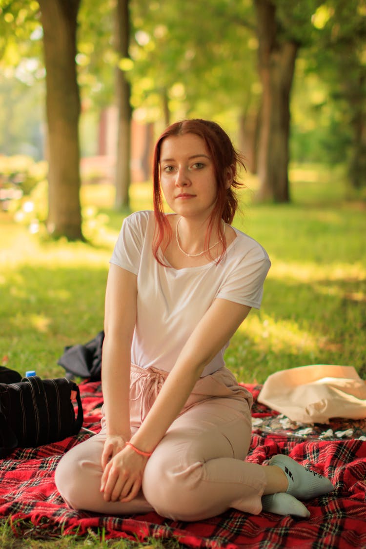 Ginger Girl Sitting On Red Blanket In Park