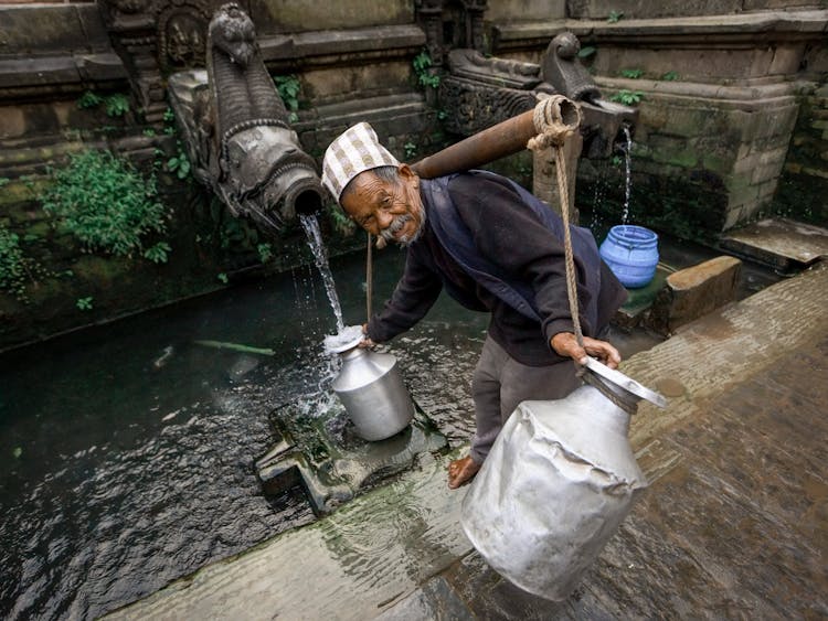 Elderly Man Pouring Water In Old Temple