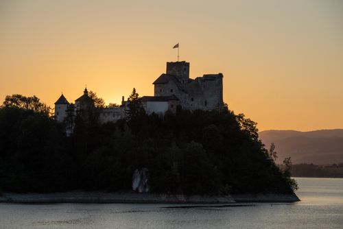 Free Stunning silhouette of Niedzica Castle against a vibrant sunset over the water in Poland. Stock Photo