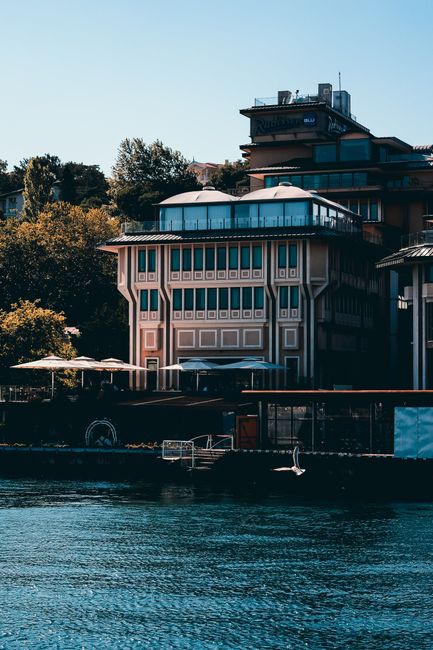 Contemporary hotel building with modern architecture by a serene body of water under a clear blue sky.