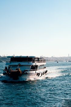 A ferry navigates through calm blue waters with a distant cityscape in the background on a sunny day.