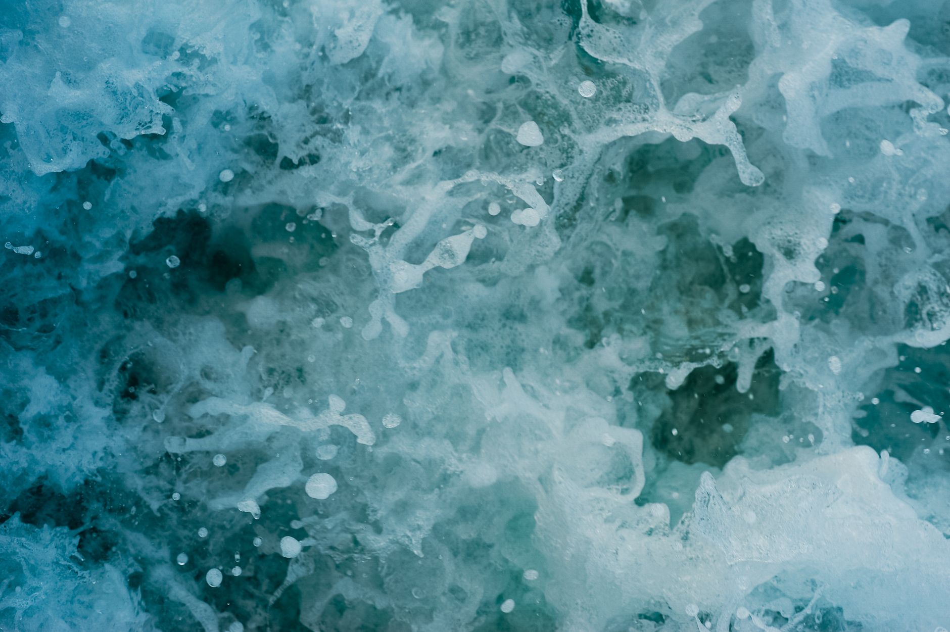 An energetic close-up of ocean waves splashing with foamy textures and vibrant aqua hues.