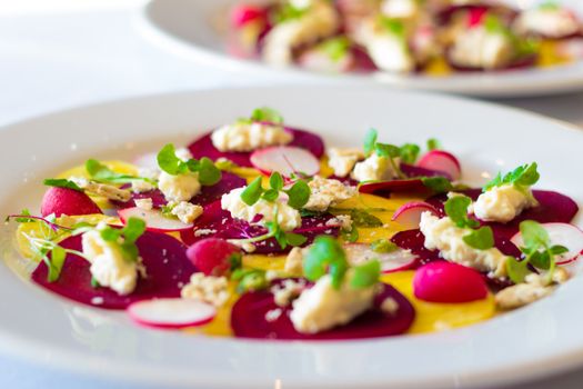Close-up of a colorful beetroot salad with cheese and fresh greens served on a white plate.