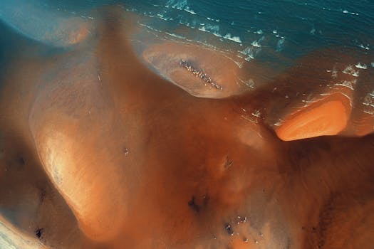 Stunning aerial view of a red sandy beach meeting the turquoise ocean waves.