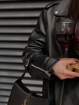 Close-up of a woman in a black leather jacket holding red wine glasses, showcasing urban elegance.