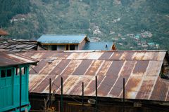 Rustic metal-roofed houses in Manali, nestled against lush green mountains under a blue sky.
