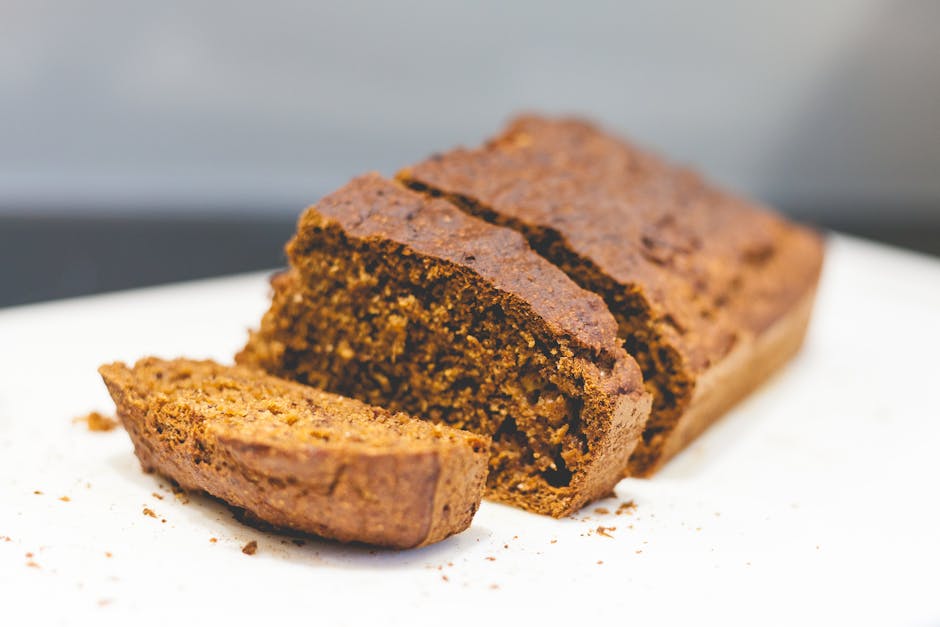A sliced loaf of protein banana bread on a wooden cutting board, showing a moist golden-brown crumb studded with chopped walnuts.