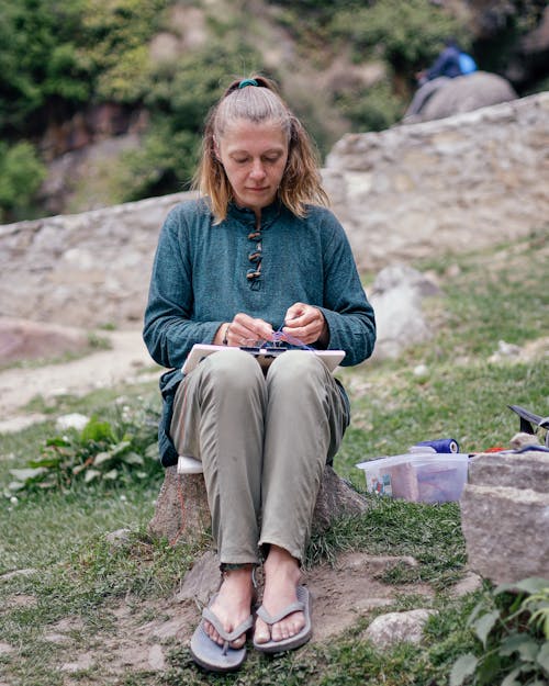 Woman in Blue Long Sleeve Shirt and Gray Pants Sitting on Gray Rock