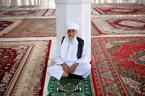 Man in White Long Sleeves and Pants Sitting on Green and White Carpet