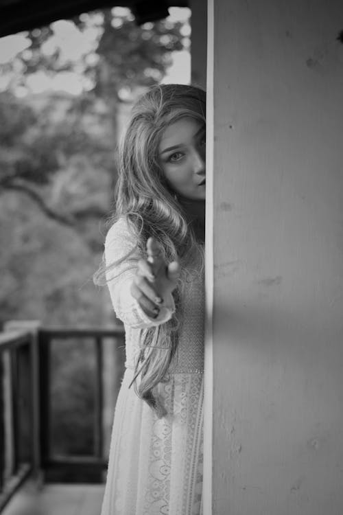 Grayscale Photo of Woman Standing Behind Wall