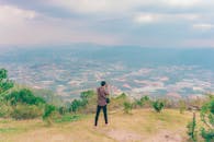 一个人在多云的天空下，俯瞰广阔的农田和山丘，拍下照片