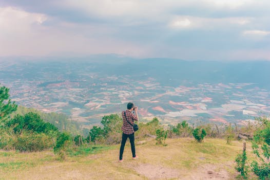 一个人在多云的天空下，俯瞰广阔的农田和山丘，拍下照片