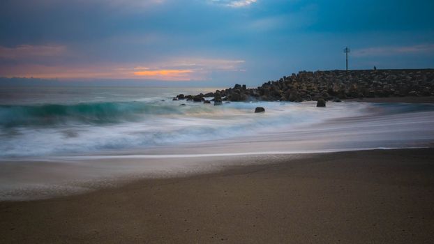 Peaceful seascape with tranquil waves and vibrant sunset over a sandy beach.