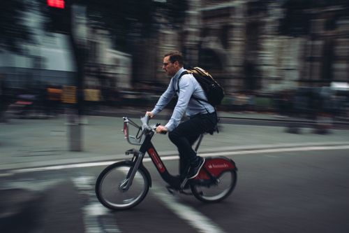 Free A man with a backpack rides a bicycle through a busy, blurred street in London, capturing dynamic city life. Stock Photo