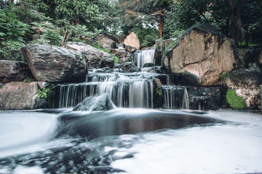 Tranquil waterfall cascading over rocks in a serene garden in London, perfect for nature lovers.