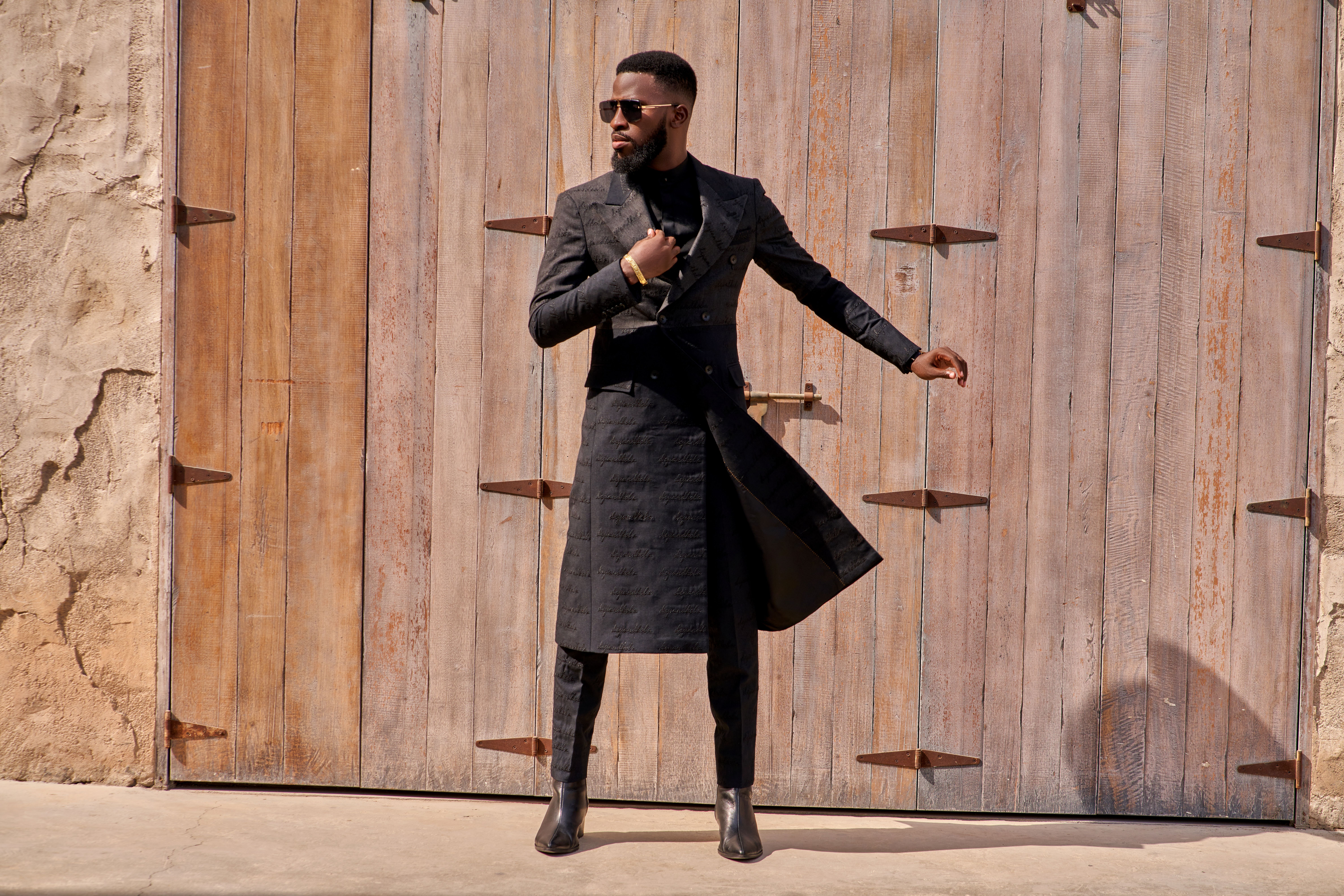 Confident man in trendy black overcoat with wooden wall backdrop in Dubai.