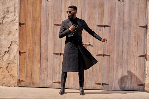 Man in Black Coat Standing Beside Brown Wooden Wall