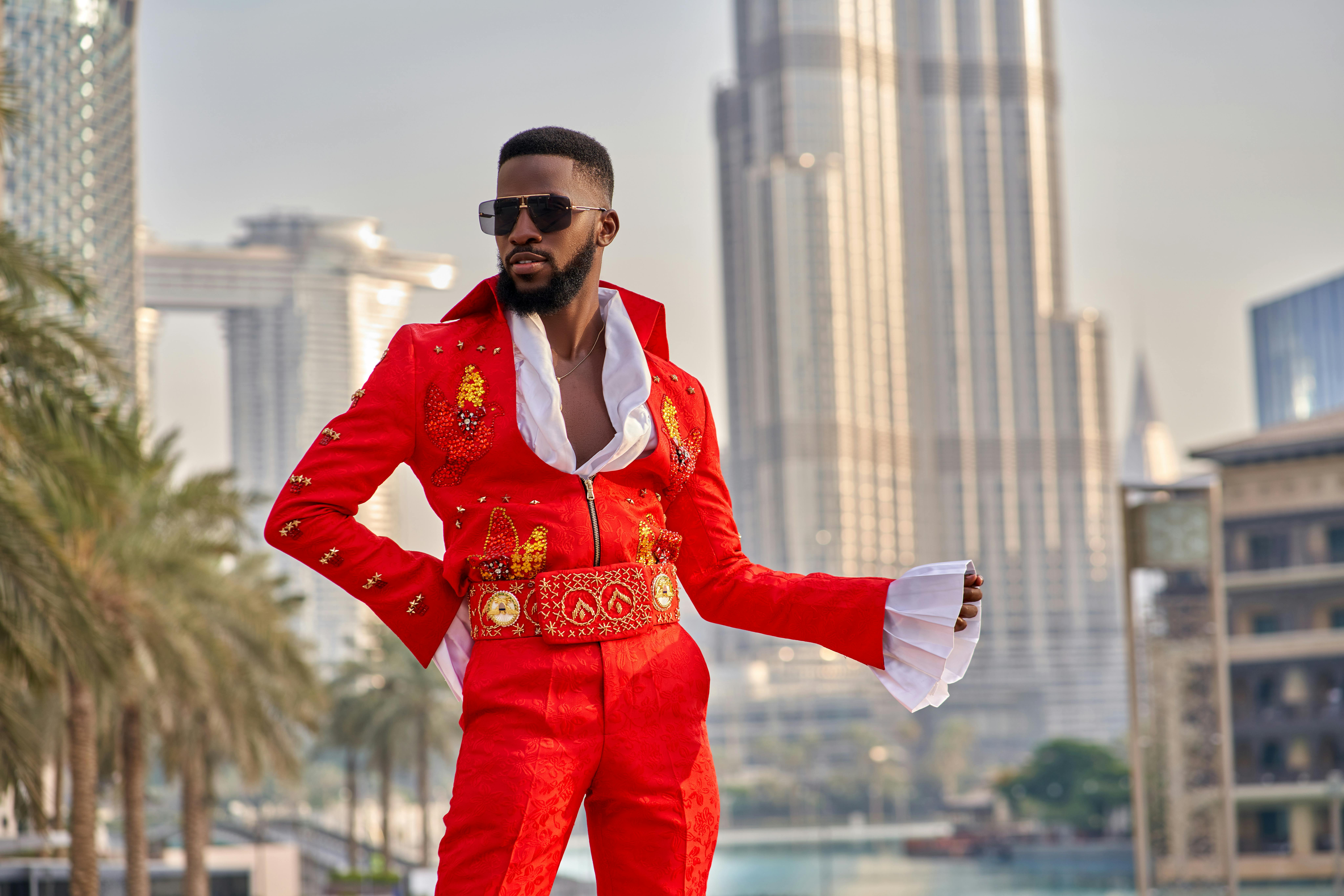 luxury abaya brands dubai - Man in vibrant red fashion outfit posing stylishly with Dubai skyscrapers in the background.