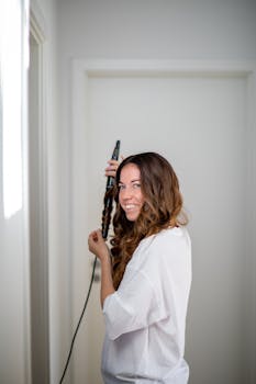 Young woman curls brown hair using styling tool indoors.
