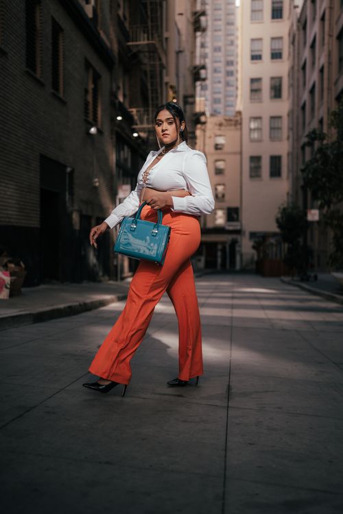 Free Fashionable woman in red pants and holding blue bag in city alley. Stock Photo