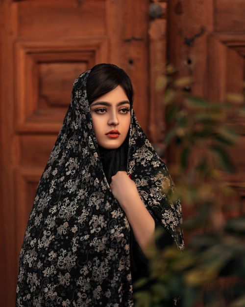 Free Elegant portrait of a woman in a floral patterned hijab against a wooden backdrop, evoking cultural beauty. Stock Photo