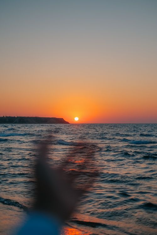 Free Capture of a vibrant sunset over the ocean with an outstretched hand in view, creating a sense of depth and wonder. Stock Photo