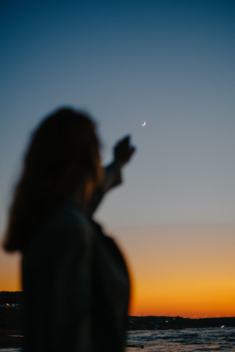 Woman Silhouette Pointing At Moon At Sunset