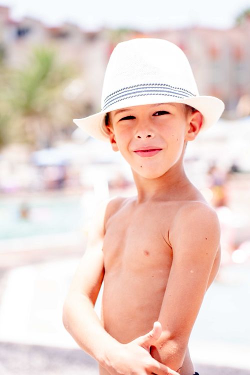 Free Boy in a white hat enjoying a topless, sunny beach day, smiling confidently. Stock Photo