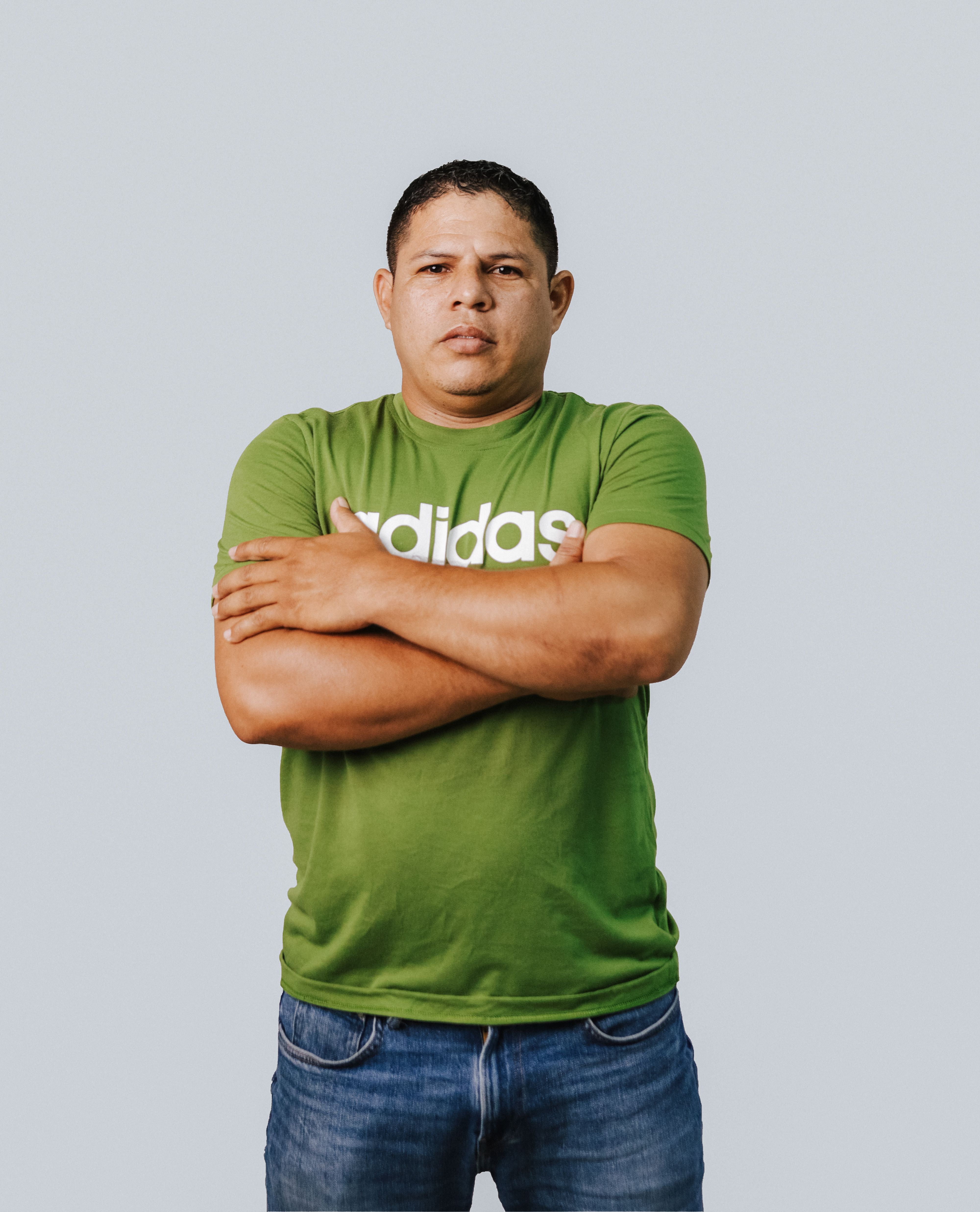 A man in a green t-shirt stands confidently with crossed arms in a studio setting.