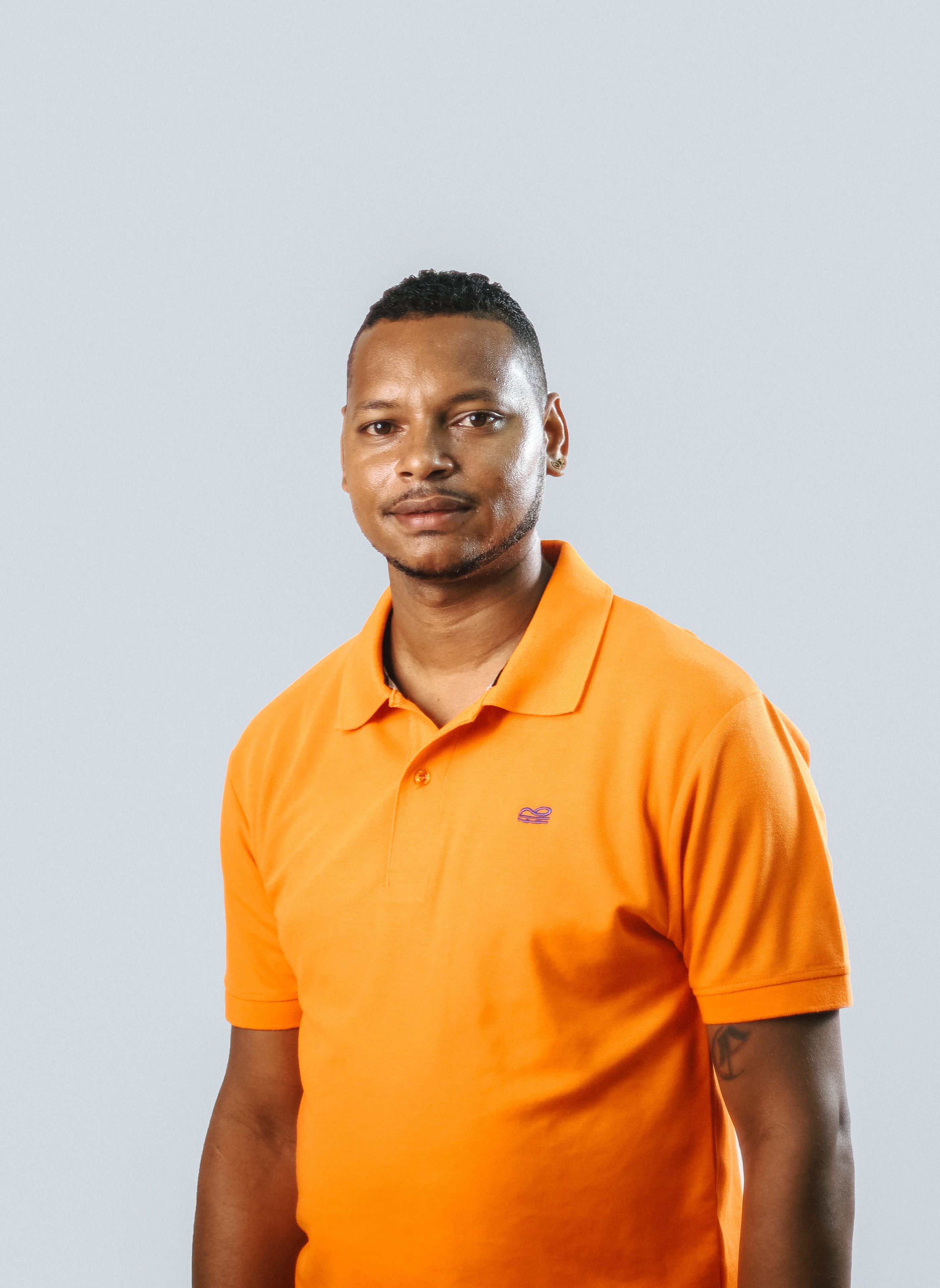 Retrato em estúdio de um homem usando uma camisa polo laranja contra um fundo cinza.