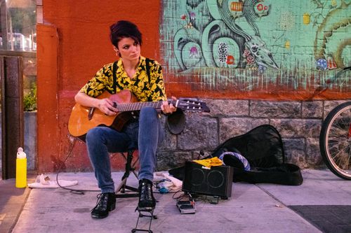 Free A street musician playing guitar by a graffiti-covered wall, adding urban charm. Stock Photo