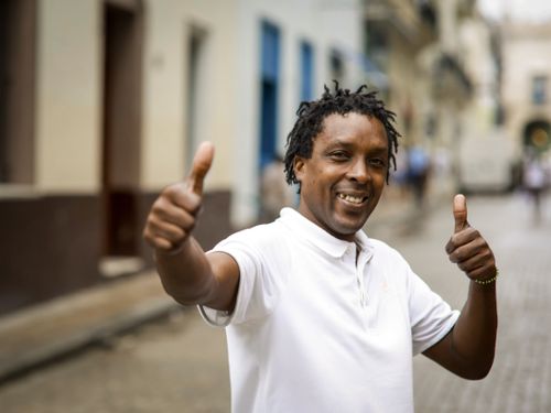Free Smiling man in a white polo shirt gives thumbs up gesture on a city street. Stock Photo