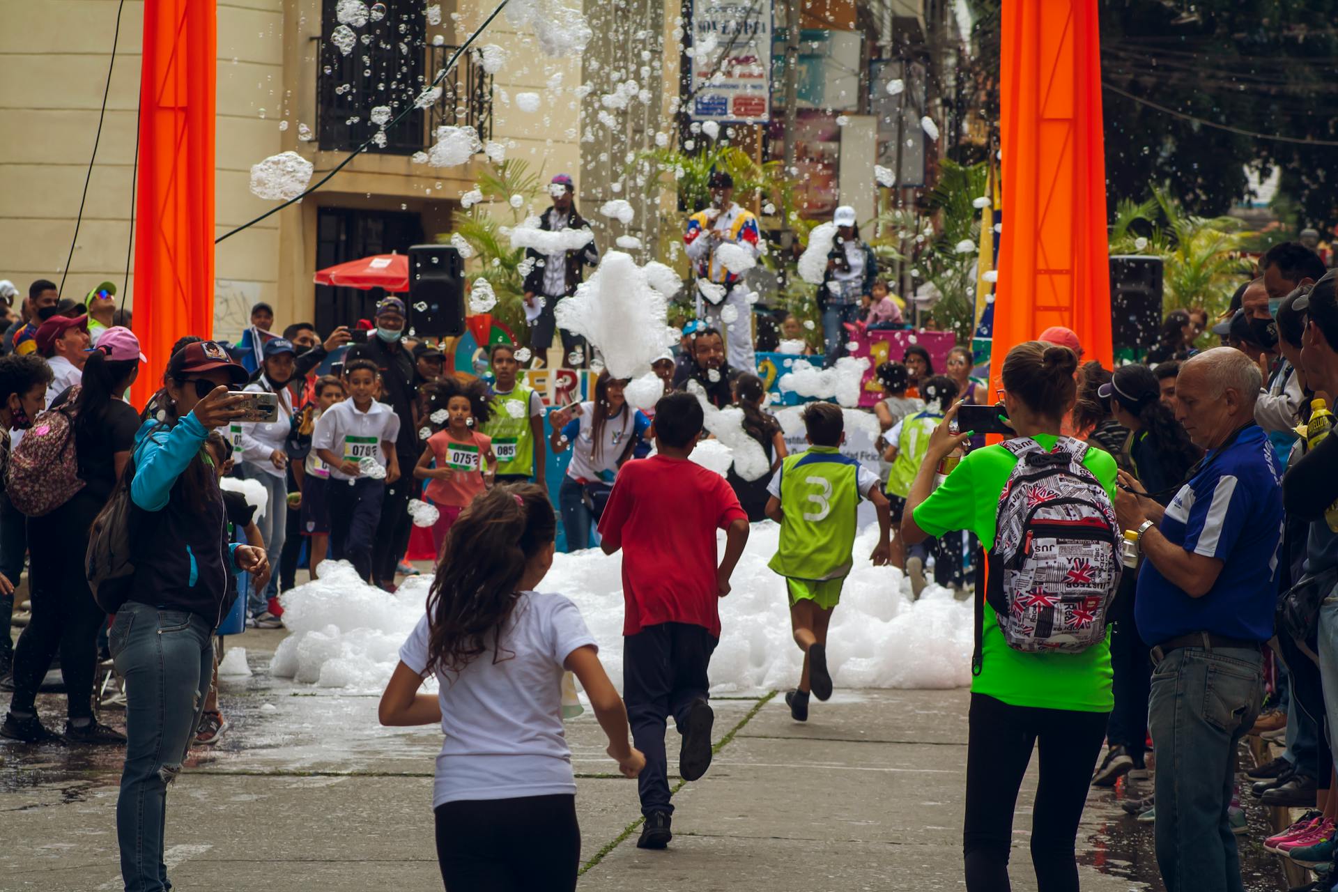 Vibrant street event with children running through foam in Venezuela.
