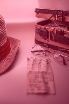 Still life of travel items with a vintage touch and pink overlay, including glasses and a hat.