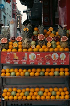 A colorful display of fruits including pineapples, grapefruits, and oranges at an urban market stall.