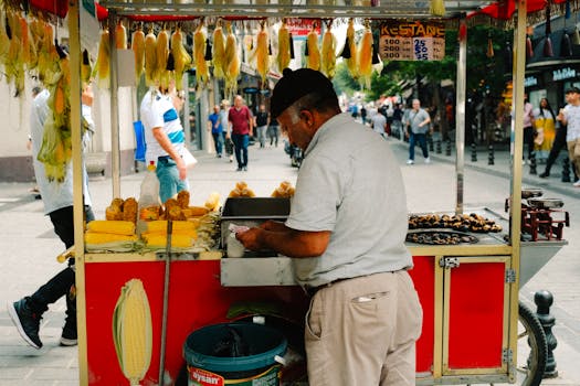 A street vendor in a bustling market selling corn and chestnuts from a stall.
